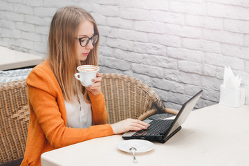 Young girl freelancer working on a laptop. Blonde girl in a cafe with a laptop and a cup of coffee