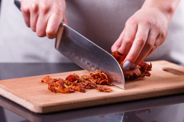 young woman in a gray apron cuts roasted bacon