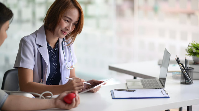 Asian Woman Doctor With Tablet Talking To Male Asian Patient In Office