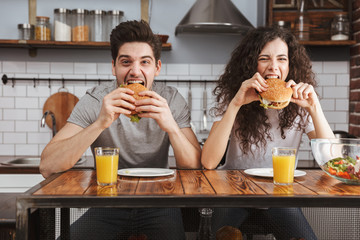 Cheerful couple eating burgers at the kitchen