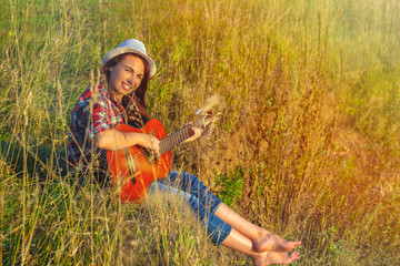 Beautiful, happy woman in the summer in the rays of the sunset with a guitar. Concept of creative freedom, fun and summer holidays.
