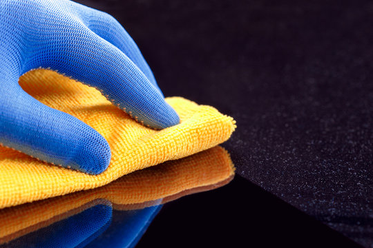 Employee hand in protective glove wiping dust layers on the furniture  with yellow dry rag.