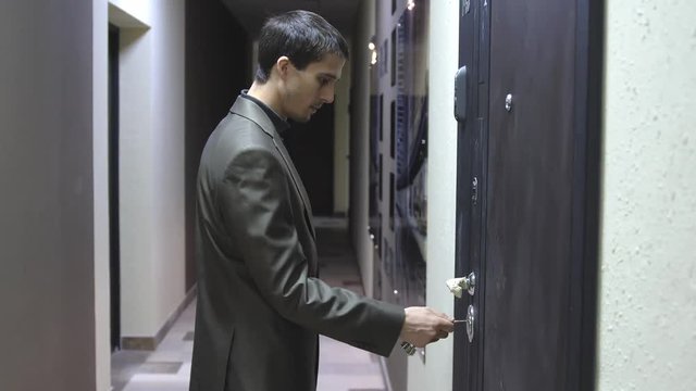 A young handsome businessman unlocks a house's door with key and enters. 3840x2160