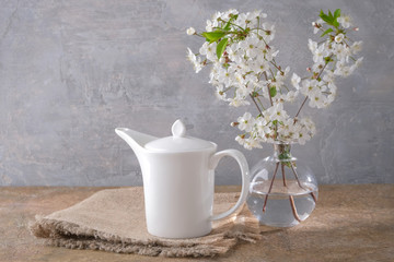 Cherry blossoms in a vase and a white teapot on a table.