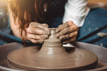 Close up mud covered hands of adult woman making clay pot on potter's wheel