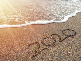Year 2020 hand written on sandy beach in sunset warm lens flare
