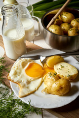 Fried egg with young potatoes with dill and milk on  wooden table