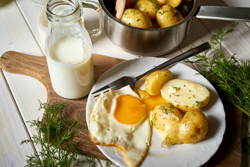 Fried egg with young potatoes with dill and milk on  wooden table