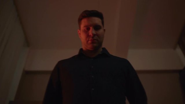 A young Caucasian in a blue shirt enters the room, sees something and goes forward. Stops, looks down and leans towards his find. Apartment, dim light. The concept of the quest. Shooting upwards