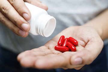 close up man hand holding a medicine, with pours the pills vitamin out of the bottle. Caring for the health care