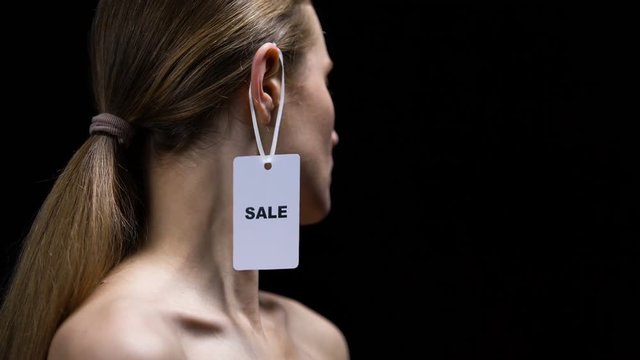Male hand putting sale tag on female ear, illegal women trafficking, sex slavery