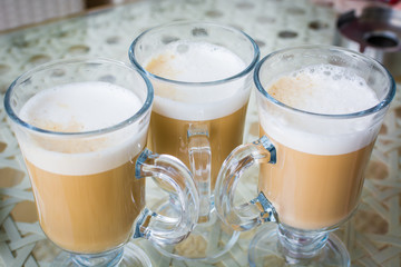 Glass glasses of hot coffee with foam stand on table.