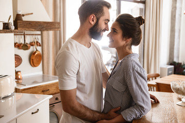 Image of adorable brunette couple in love smiling while hugging together in apartment
