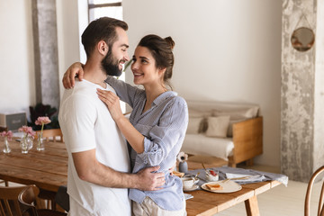 Photo of excited brunette couple in love smiling while hugging together in apartment