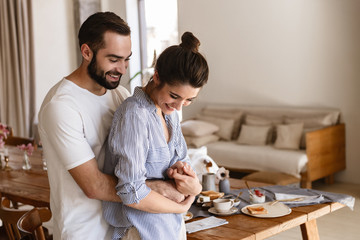Photo of joyful brunette couple in love smiling while hugging together in apartment