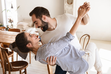 Photo of content brunette couple in love smiling while hugging together in apartment