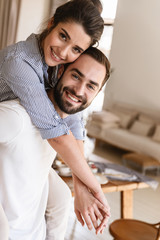 Photo of attractive brunette couple in love smiling while hugging together in apartment