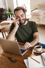 Photo of unshaved mature man using laptop and smartphone while working in flat