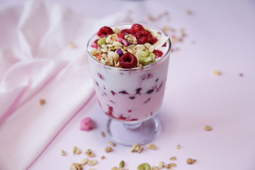Granola yogurt parfait with fresh raspberry berries on a light pink background. Healthy food. With copy space for text.