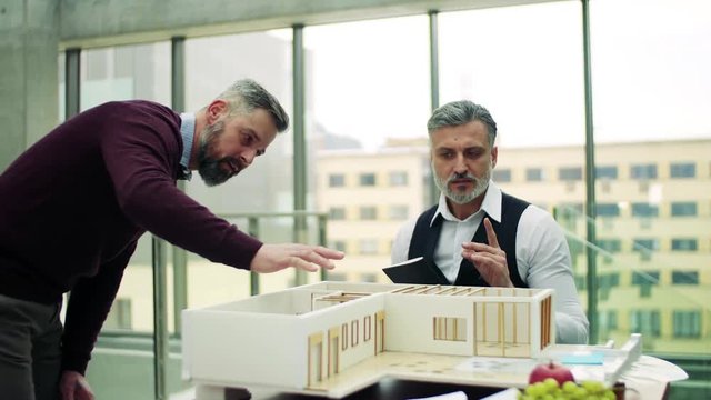 Two architects with model of a house in office, talking.