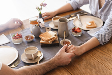 Image of happy brunette couple eating together at table while having breakfast in apartment
