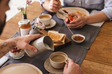 Image of modern happy couple eating together at table while having breakfast in apartment - obrazy, fototapety, plakaty