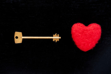 Golden key with red plush heart on black background