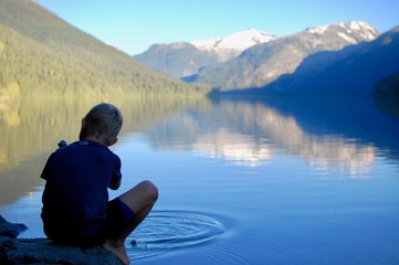Young boy uses water purifier while backpacking in the beautiful glacier mountains with a reflection in the lake in British Columbia, Canada. 