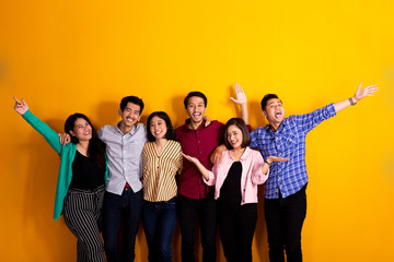 happy young asian friend raised their arm together over yellow background