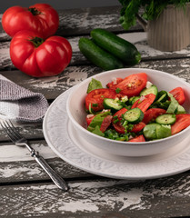 tomato and cucumber salad in white bowl on old wooden rustic backdrop, tomatoes on background