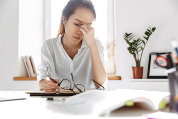 Tired asian business woman sitting by table with closed eyes