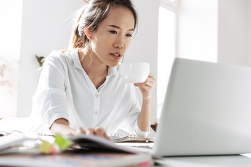 Concentrated asian business woman drinking coffee and using laptop computer