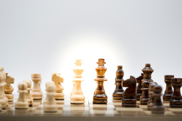 Face to face of wooden black and white chess on chess board with sunlight. Battle in game and business concept.
