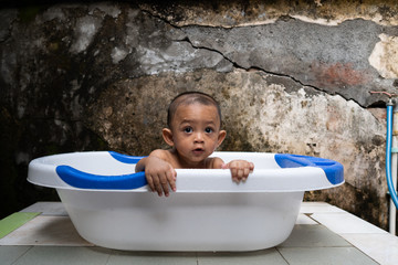 An handsome 7-month-old boy is bathing in his bathtub with an old but artistic background