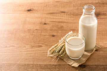 Oats milk in bottle and glass on wooden table. Copyspace