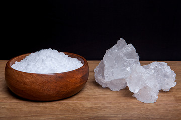 Coarse granules of natural rock or sea salt in a bowls on wooden table.