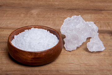 Coarse granules of natural rock or sea salt in a bowls on wooden table.