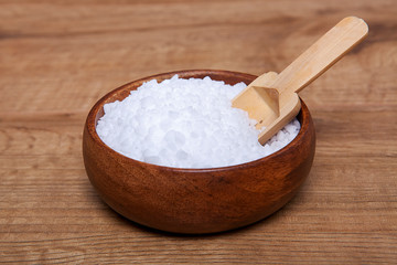 Coarse granules of natural rock or sea salt in a bowls on wooden table.