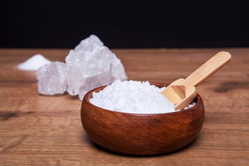 Coarse granules of natural rock or sea salt in a bowls on wooden table.