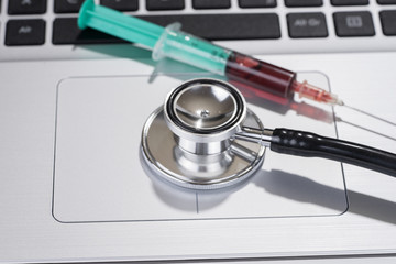 Syringe and stethoscope laying on laptop keyboard. Medicine industry concept