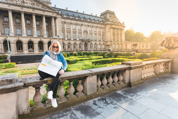 Obraz premium Young girl tourist sits on the background of the Royal Palace in Brussels and looks into the city map, Belgium