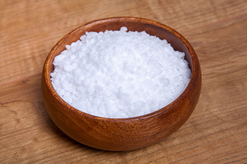 Coarse granules of natural rock or sea salt in a bowls on wooden table.