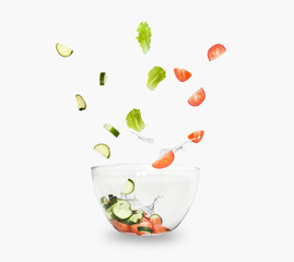 glass salad bowl in flight with vegetables: tomato, cucumber and leaf salad. Isolated on white background. healthy diet