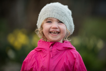 Little girl in pink with hat laughing and making faces in a garden