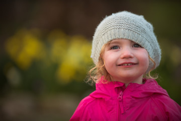 Little girl in pink with hat laughing and making faces in a garden