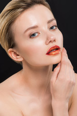 naked and attractive woman with orange lips touching face isolated on black