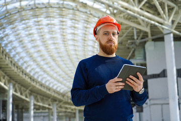 The average plan is a portrait of an adult man in a helmet checking, checking with the schedule, holding a tablet PC, horizontal, space for signature