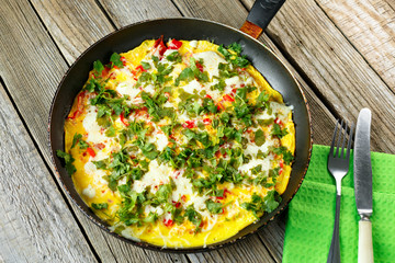 Omelette in frying pan on wooden table. Knife and fork on green towel. Vegetarian lifestyle.