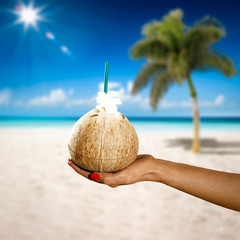 Fototapeta na wymiar Woman hand with coconut drink. Summer sunny day on beach. 