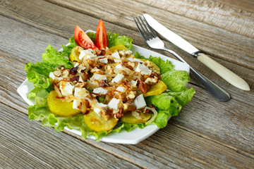 Roasted potatoes on the plate with onions cheese and nuts. Knife and fork on green towel. Vegetarian lifestyle.